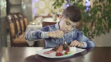 可爱的黑发小男孩喜欢吃巧克力甜点，在高档餐厅，舒适的氛围背景下，凌乱的手嘴。